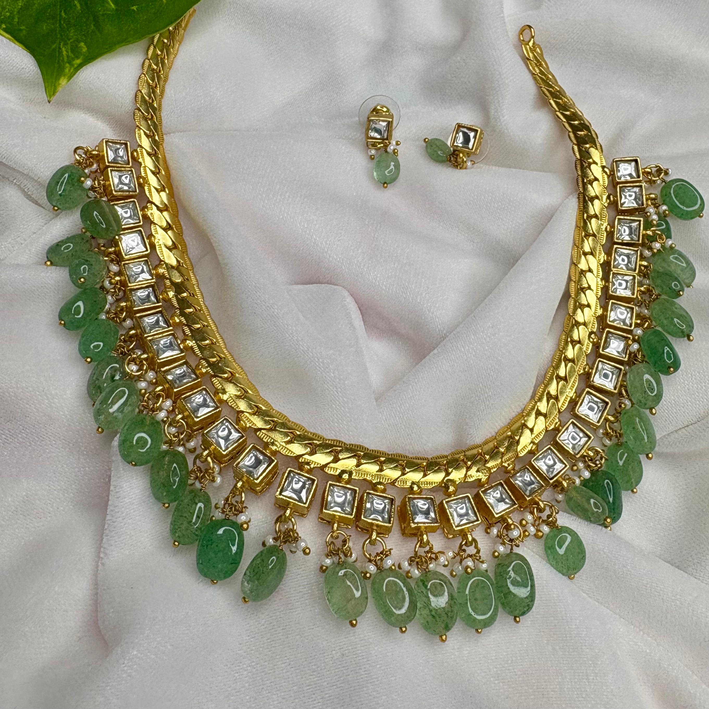 Gold necklace with green stones and matching earrings on a white fabric background