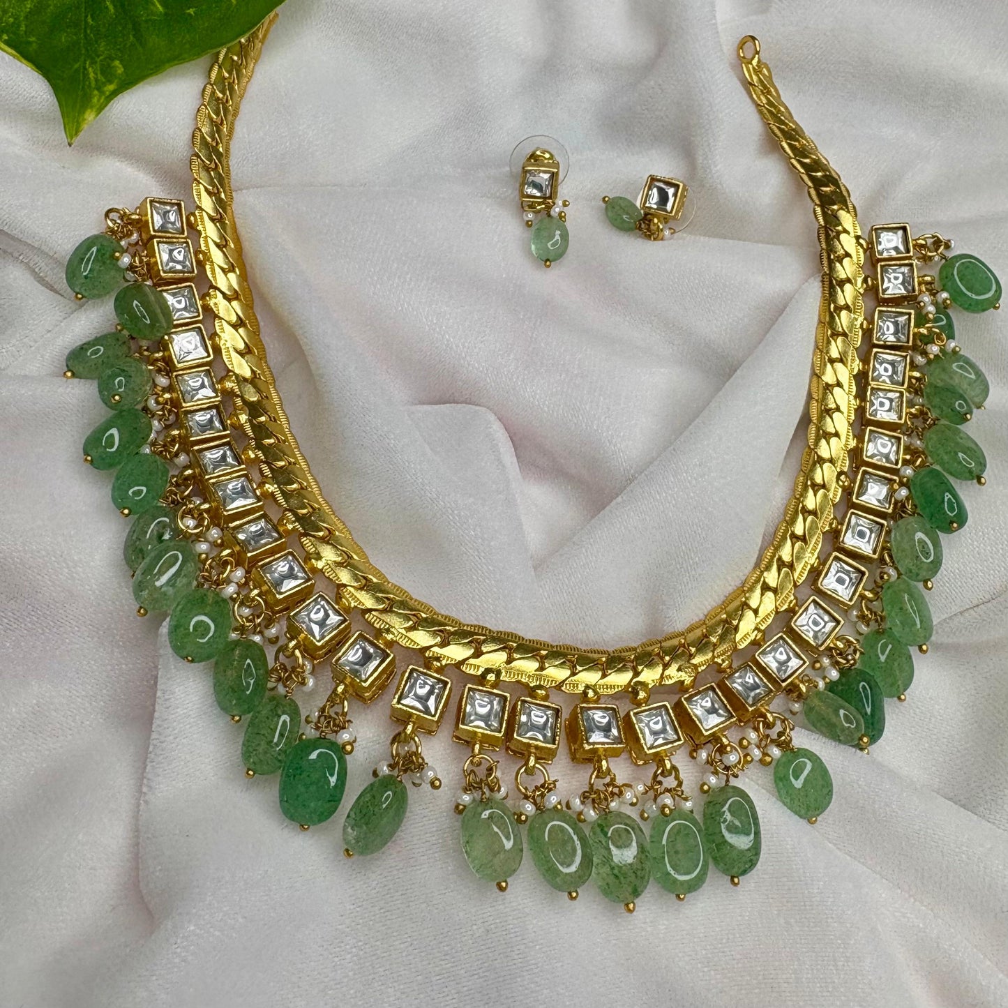 Gold necklace with green stones and matching earrings on a white fabric background