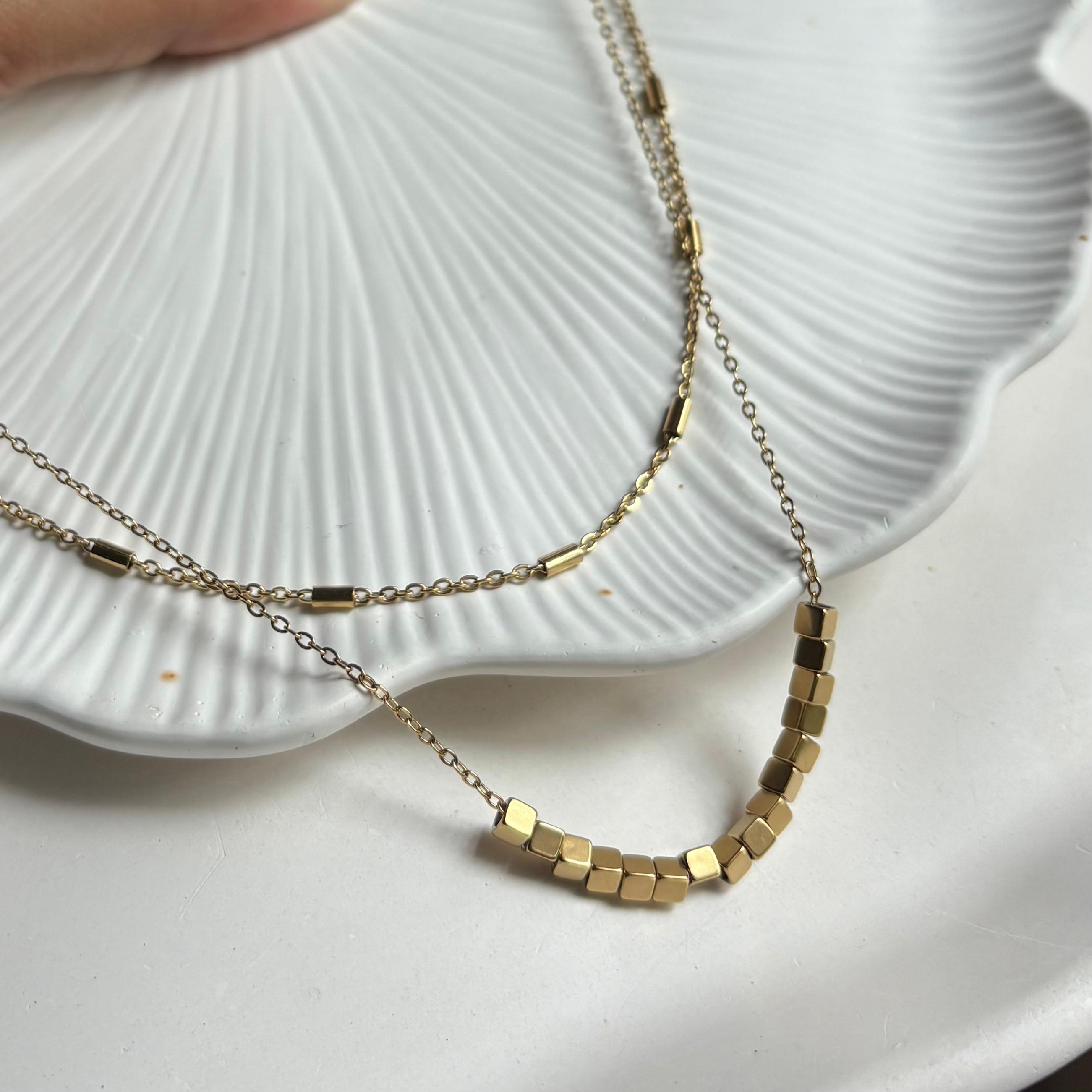 Gold necklace with hexagonal beads on a white shell background