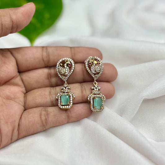 Pair of earrings with turquoise stones held between fingers on a white fabric background