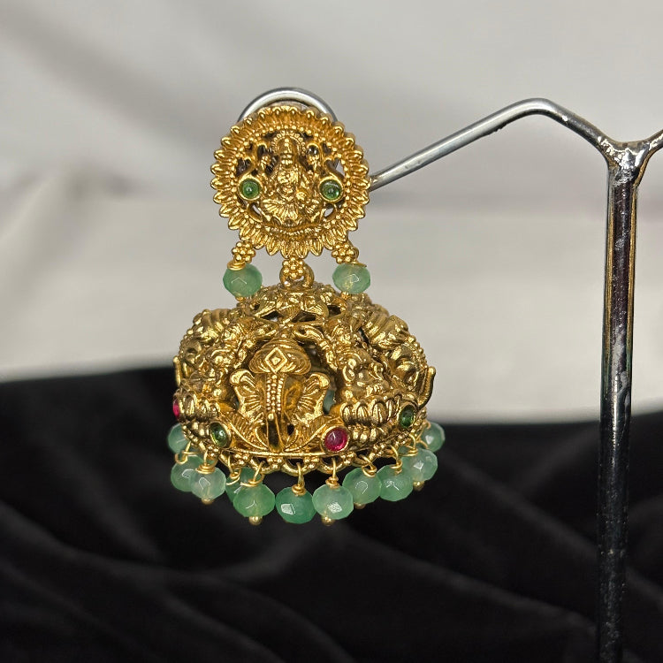 Gold earrings with green beads on a stand against a black fabric background
