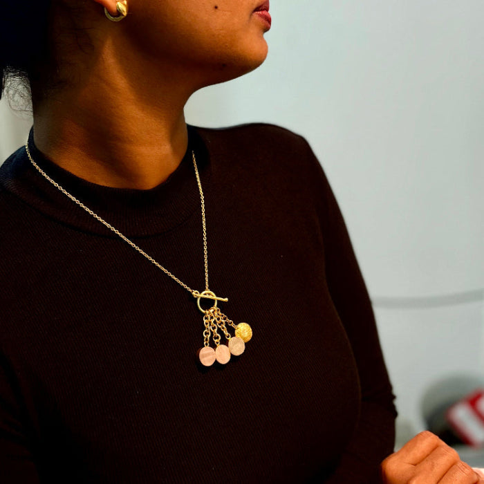 Person wearing a necklace with a pendant, standing against a plain background