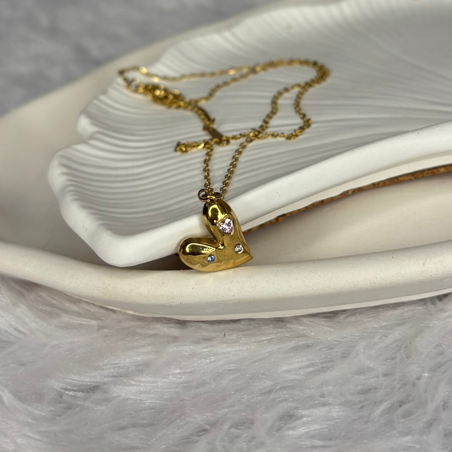 Gold heart-shaped necklace with small diamonds on a white dish.