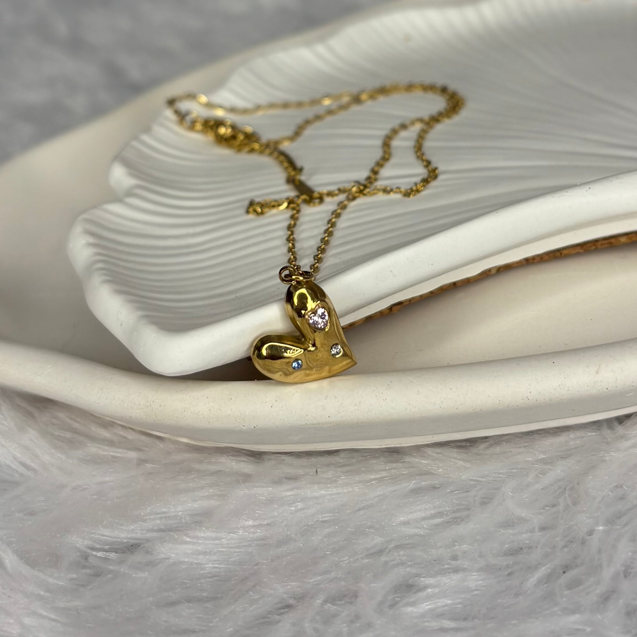 Gold heart-shaped necklace with small diamonds on a white dish.