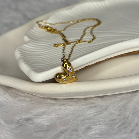 Gold heart-shaped necklace with small diamonds on a white dish.