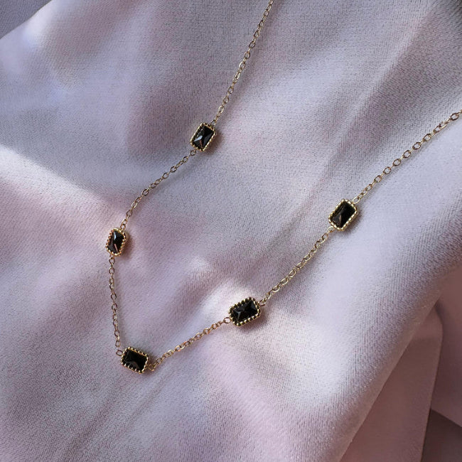 Necklace with green gemstones on a soft pink fabric background