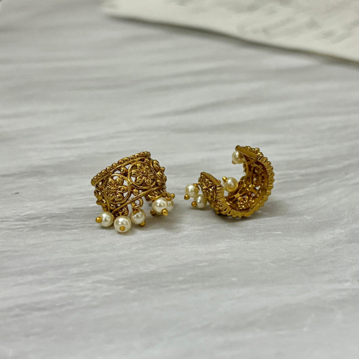 Pair of gold earrings with pearl accents on a light gray surface