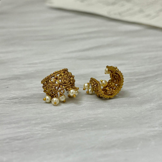 Pair of gold earrings with pearl accents on a light gray surface